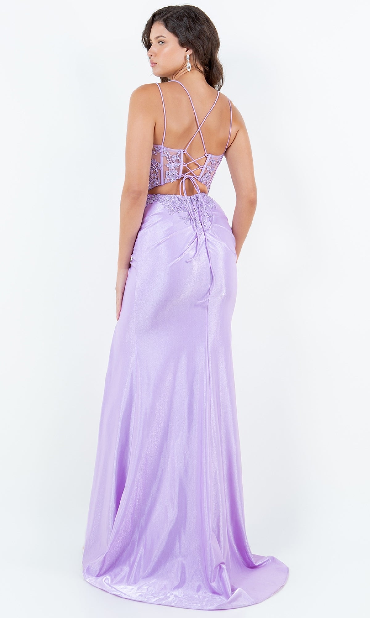 A woman stands looking over her shoulder in a floor-length, shimmery Lace-Up Lilac Prom Gown: Cinderella Couture 8185J with an open back.